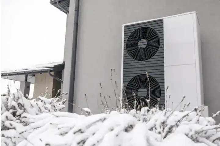 heat pump in front of a house in winter, covered with snow