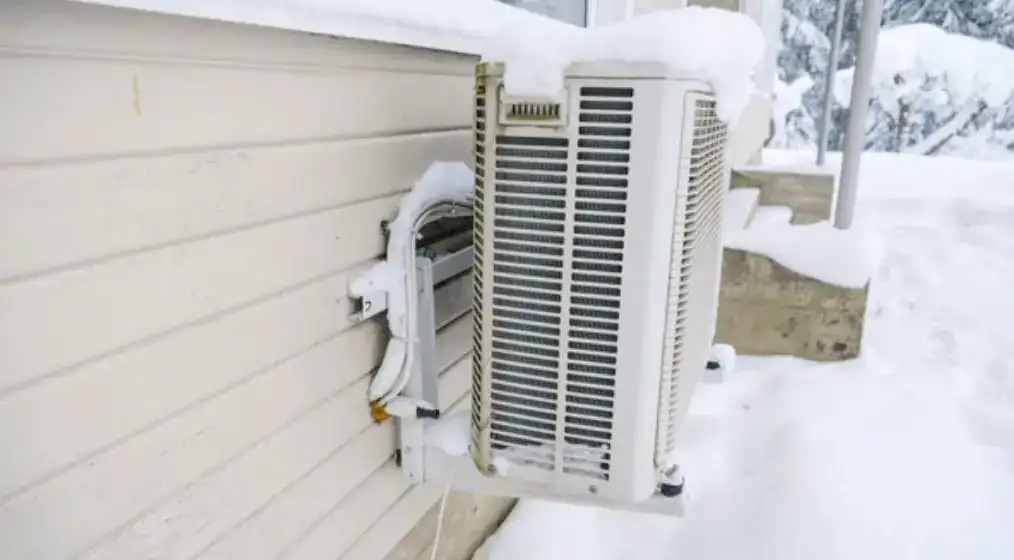 air source heat pump next to a wall, covered in snow, functioning in winter